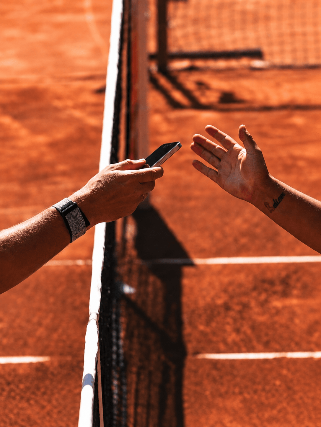 A phone passed between two hands over a clay court